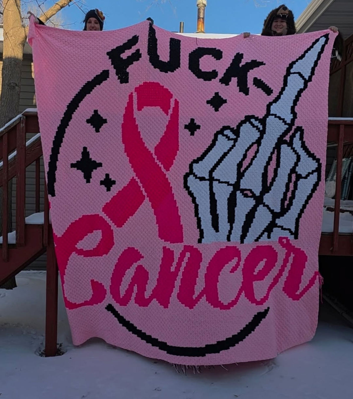 Finished Fuck Cancer crochet blanket held outdoors featuring pink ribbon awareness design and skeleton middle finger