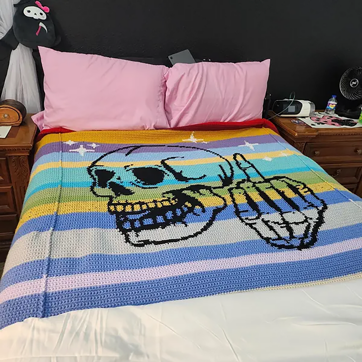 Finished Middle Finger Skeleton crochet blanket on a bed, made by a customer in colorful striped yarn