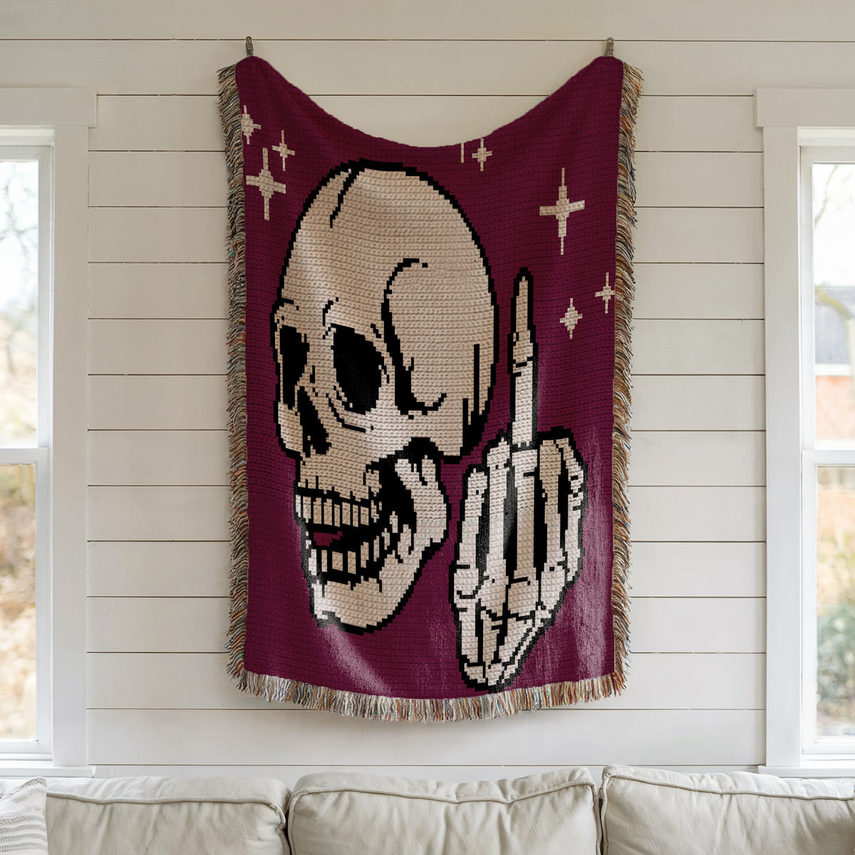 Middle Finger Skeleton crochet blanket hanging on a white wall above a sofa, showing white skull and raised middle finger on purple background