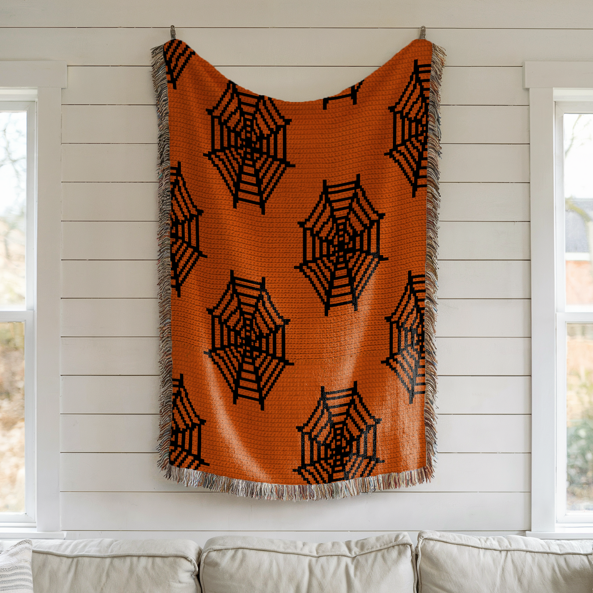 Orange spider web crochet graphgan blanket hanging on a light wall
