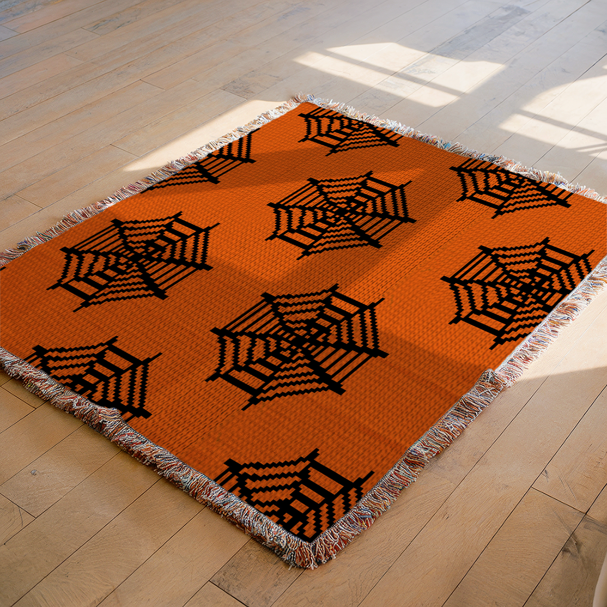 Orange and black spider web crochet blanket displayed on a wooden floor